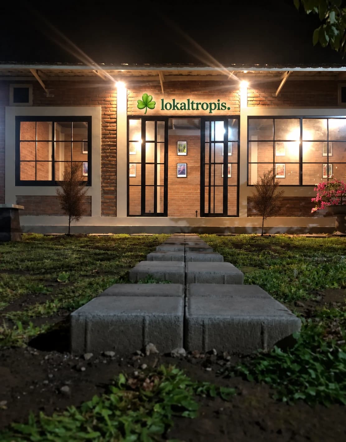 The Lokaltropis storefront at night, warmly lit behind a row of stepping stones.